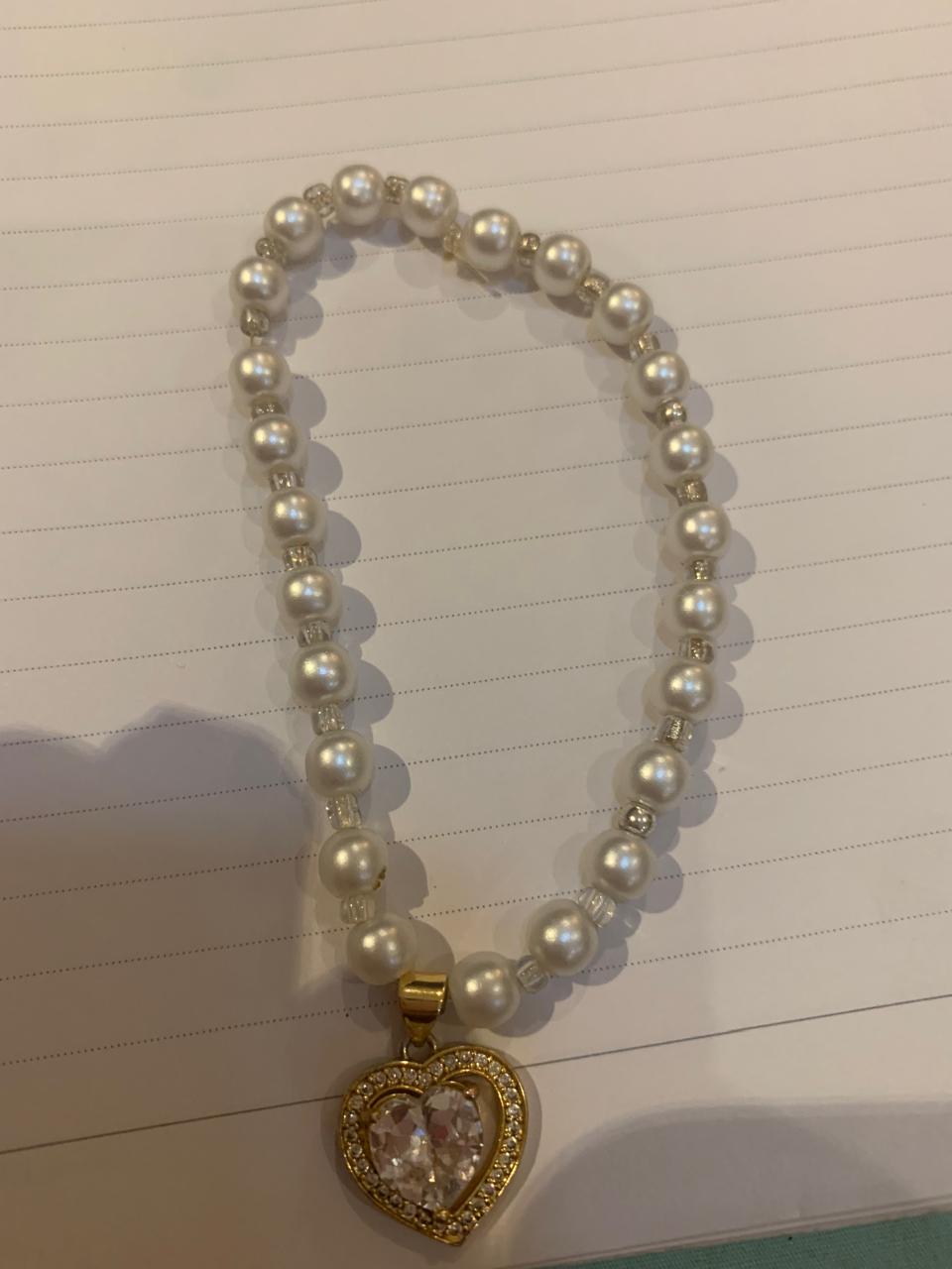 Pulsera de bisutería blanca con dije de corazón dorado.